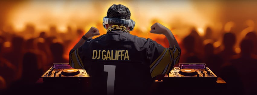 DJ Galiffa raising both arms behind the decks in front of a packed crowd